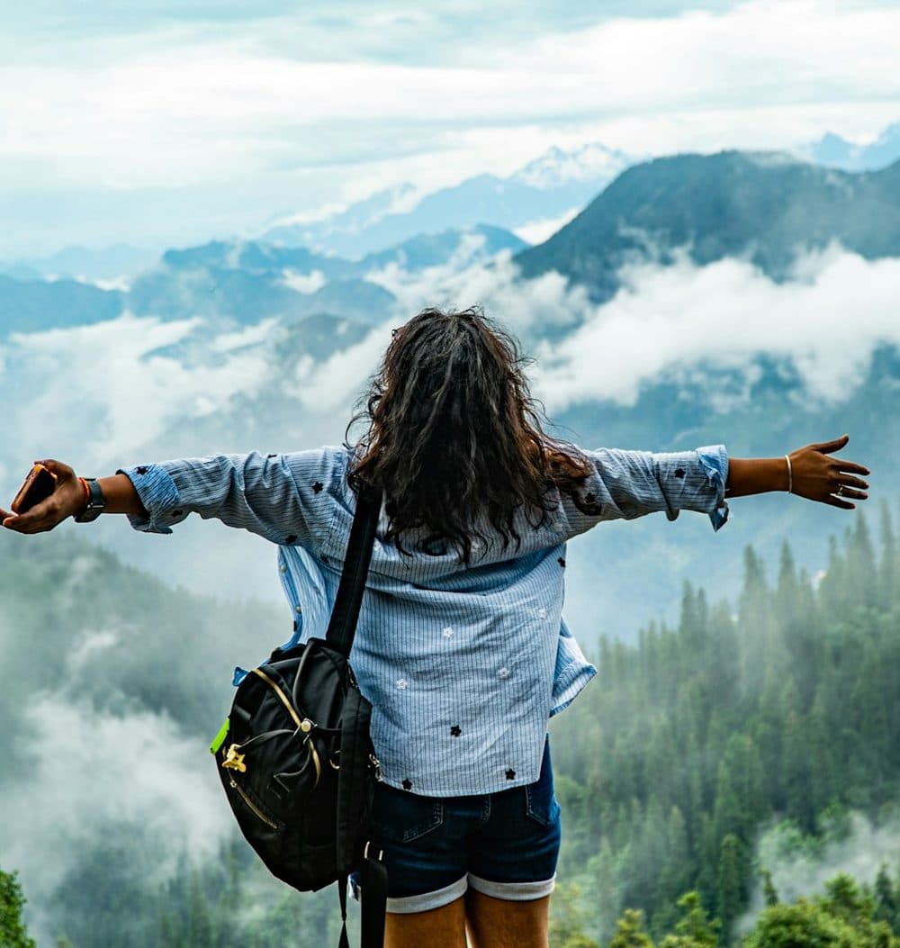 Traveller with a backpack, arms open above the mountains